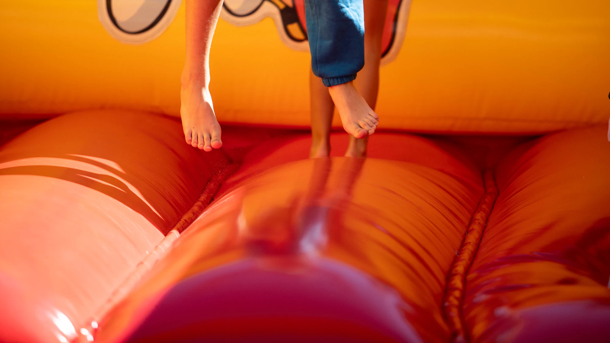 Children bouncing barefoot on a bright orange bouncy castle in golden light