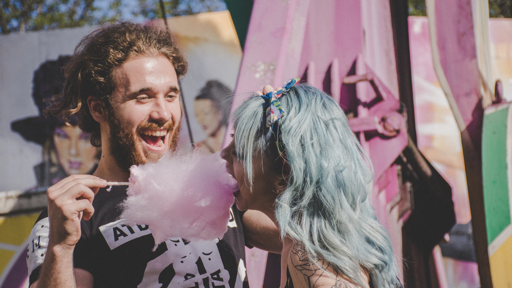 Couple laughing while sharing pink candy floss at the fair