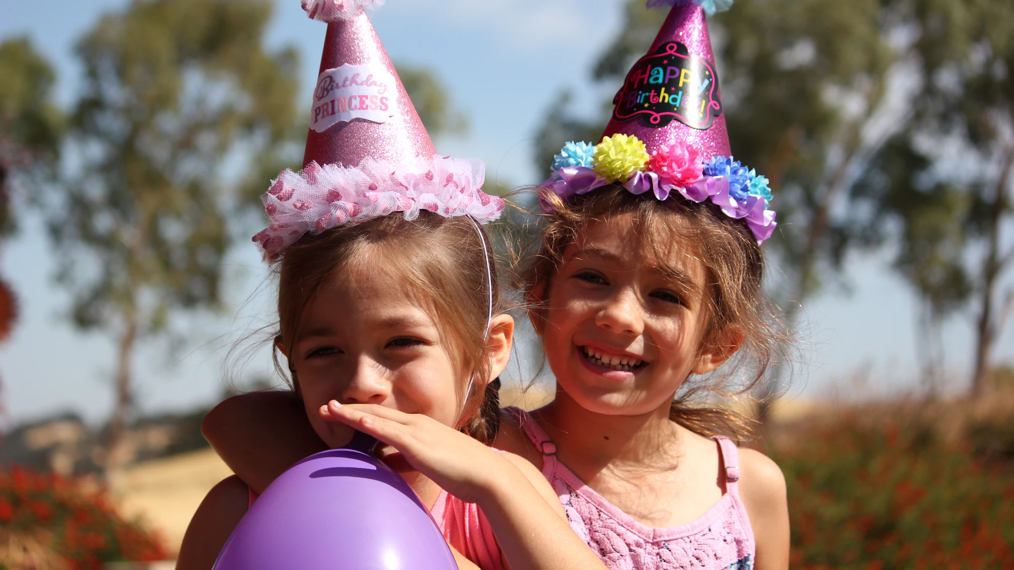 Two girls in party hats laughing with balloons outdoors