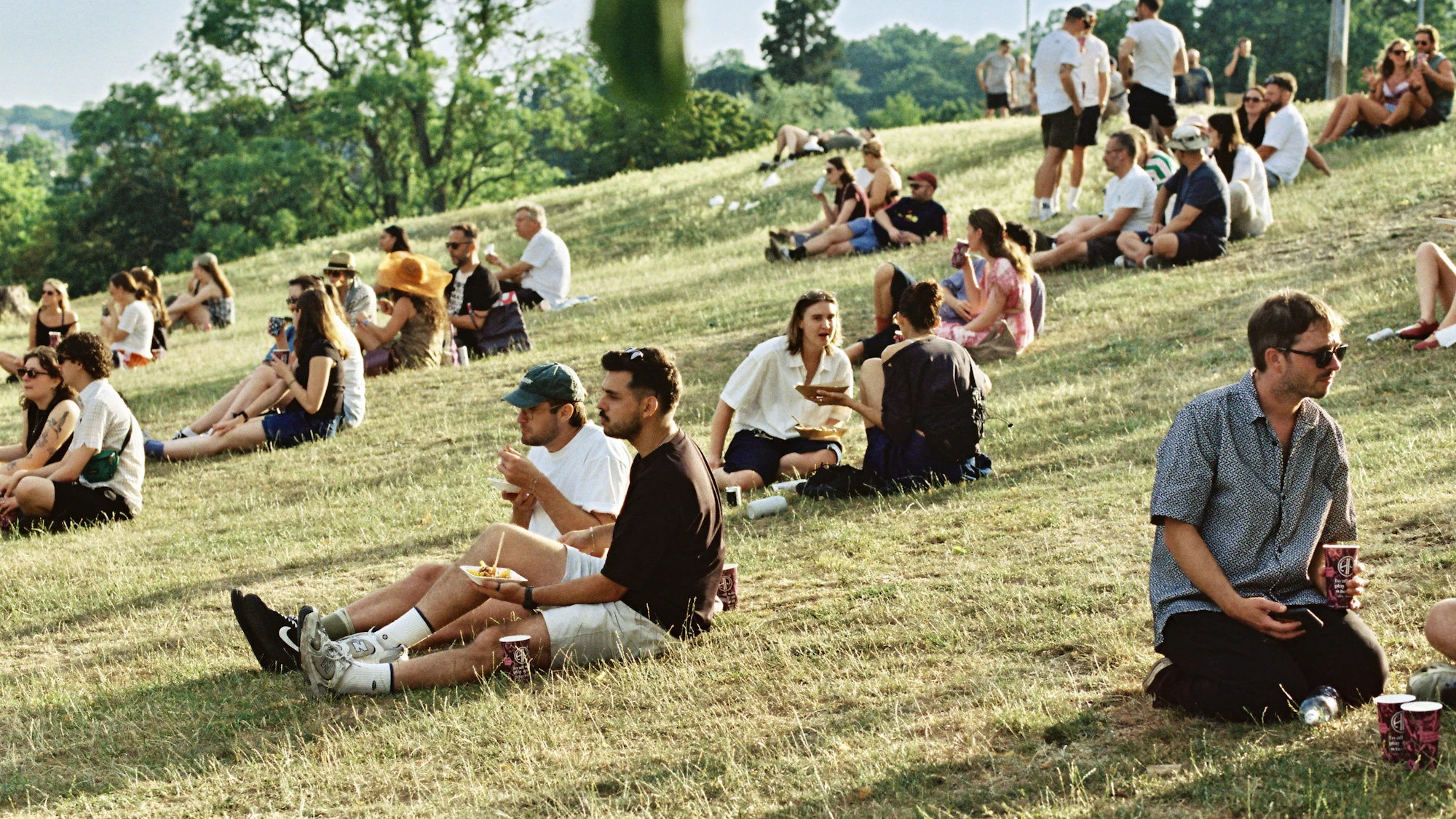 Festival-goers relaxing on a golden grassy slope at a summer village event